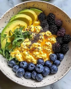 Breakfast bowl with scrambled eggs, avocado, and berries on a wooden table