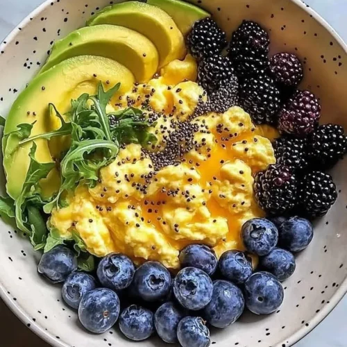 Breakfast bowl with scrambled eggs, avocado, and berries on a wooden table