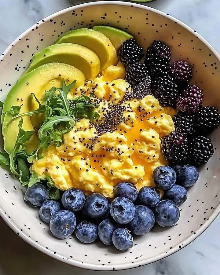 Breakfast bowl with scrambled eggs, avocado, and berries on a wooden table