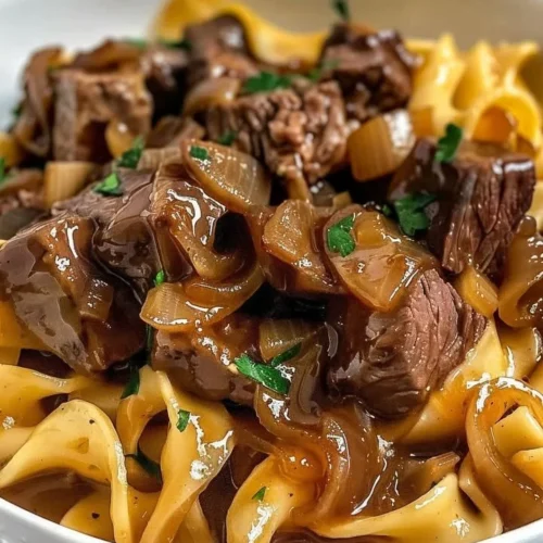 A hearty plate of French onion beef and noodles garnished with fresh herbs.