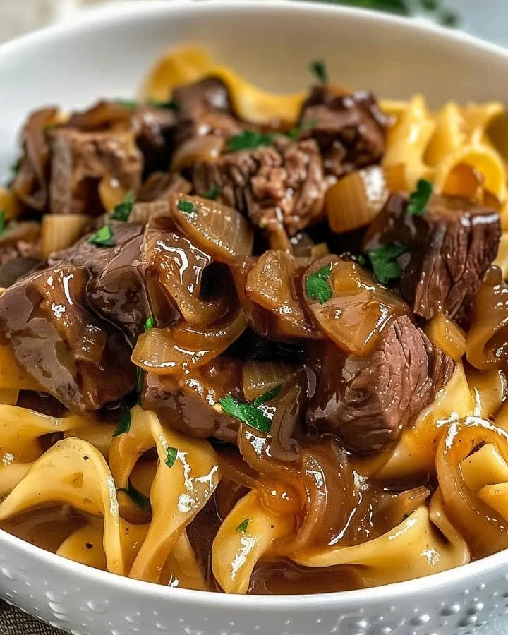 A hearty plate of French onion beef and noodles garnished with fresh herbs.