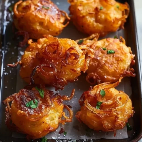 Crispy golden onion fritters served on a white plate with dipping sauce.