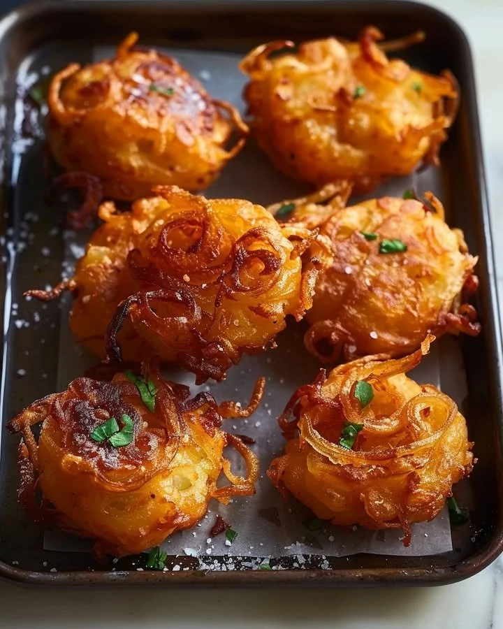 Crispy golden onion fritters served on a white plate with dipping sauce.