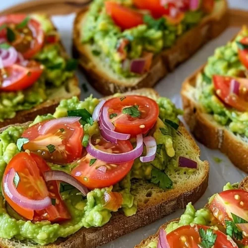 Smashed avocado bruschetta topped with fresh herbs and spices on toasted bread.